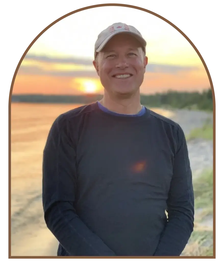 Man in cap smiling at sunset by water.