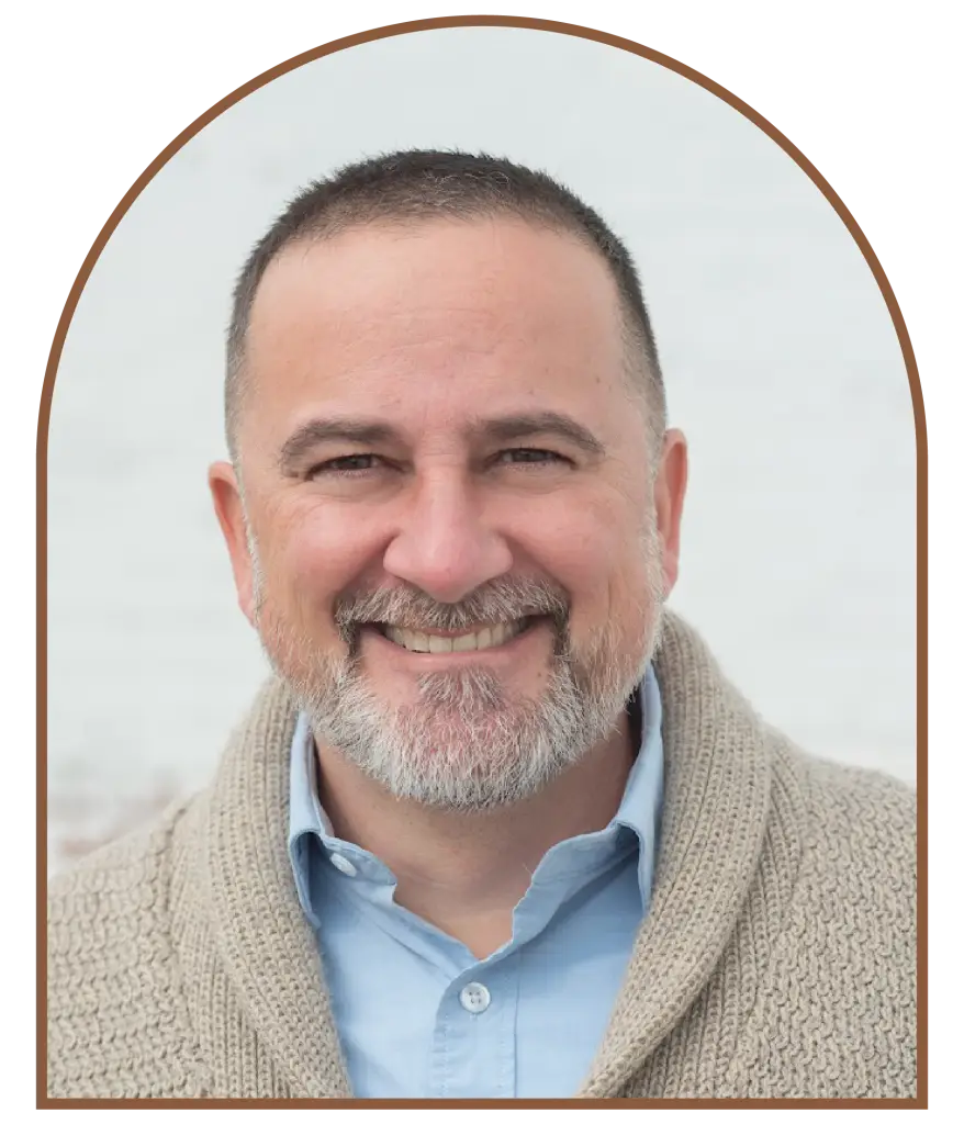 Portrait of smiling man with beard wearing blue shirt and tan cardigan.