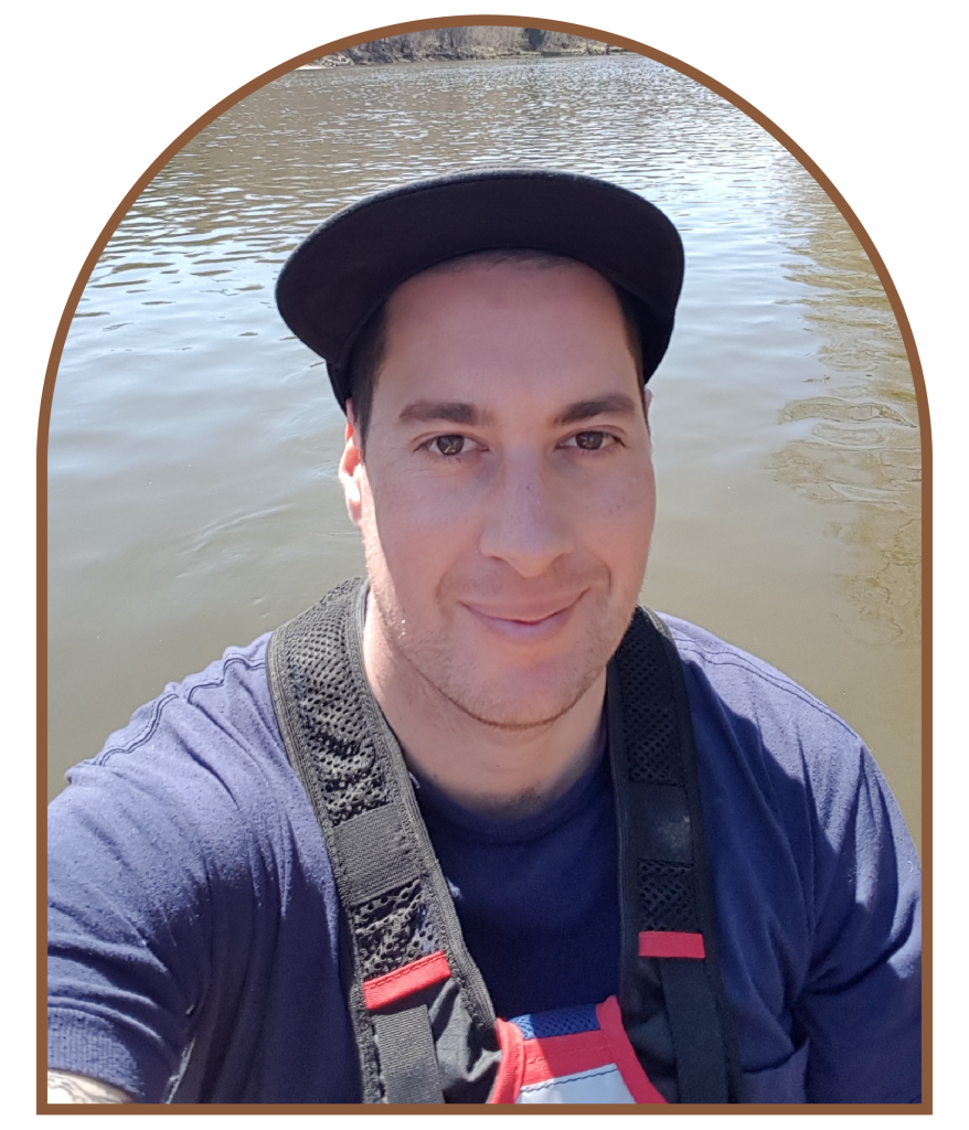 A photo of a man with a hat on looking at the camera with water in the background