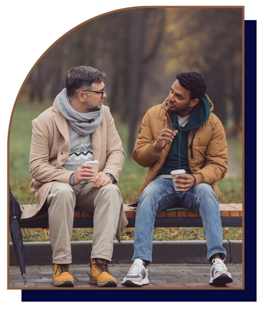 Two men having conversation on bench with coffee cups.
