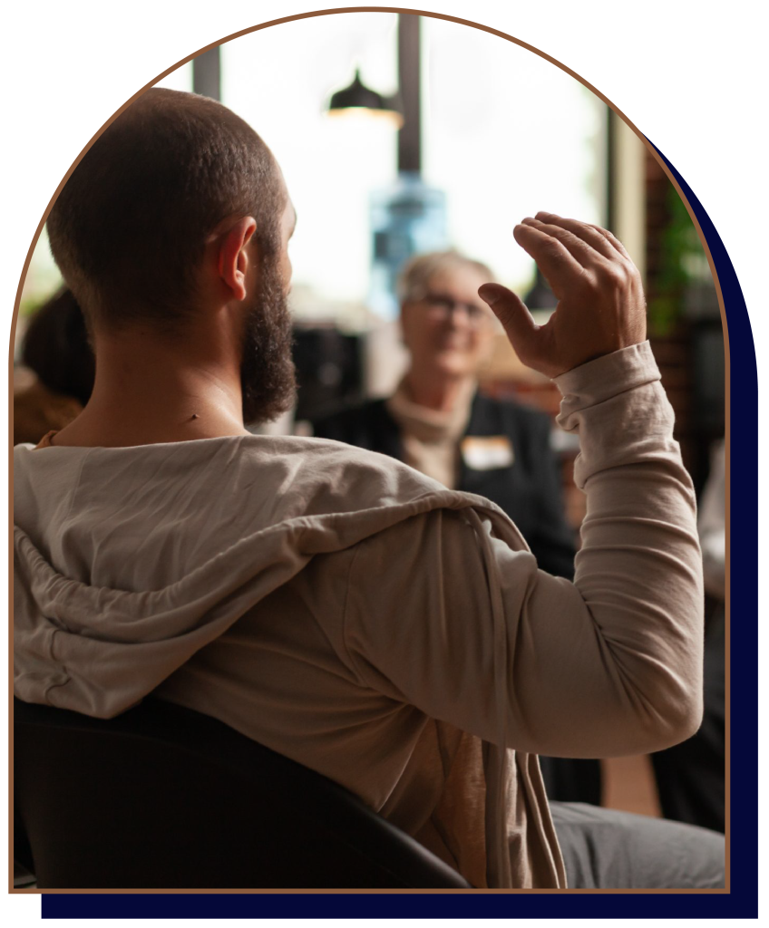 Man with beard gesturing while speaking to others indoors.