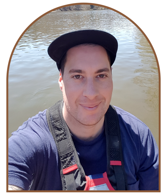 A photo of a man with a hat on looking at the camera with water in the background