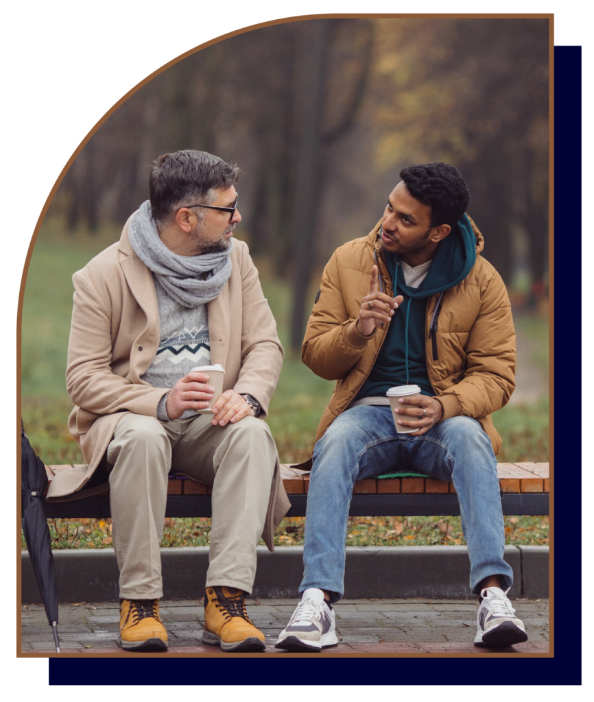 Two men having conversation on bench with coffee cups.